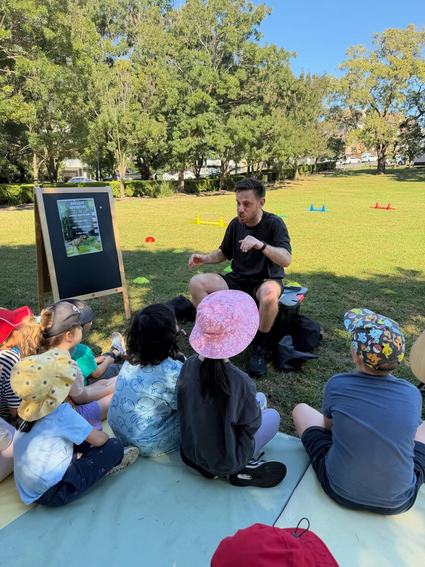 A Mini Missions coach telling a dinosaur adventure story to a group of children in a park
